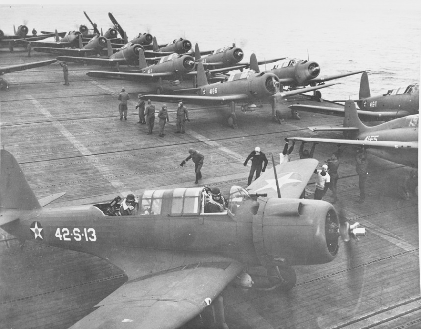 Flight deck operations, 19 November 1941, showing Vought SB2U "Vindicators" of VS-41 and VS-42 getting ready for a patrol flight, and a Grumman F4F-3 "Wildcat" of VF-41 (right). Note marking schemes in use on planes, white codes, crew of plane in foreground in cold weather gear. Description: NHC Catalog #: 80-G-391590 